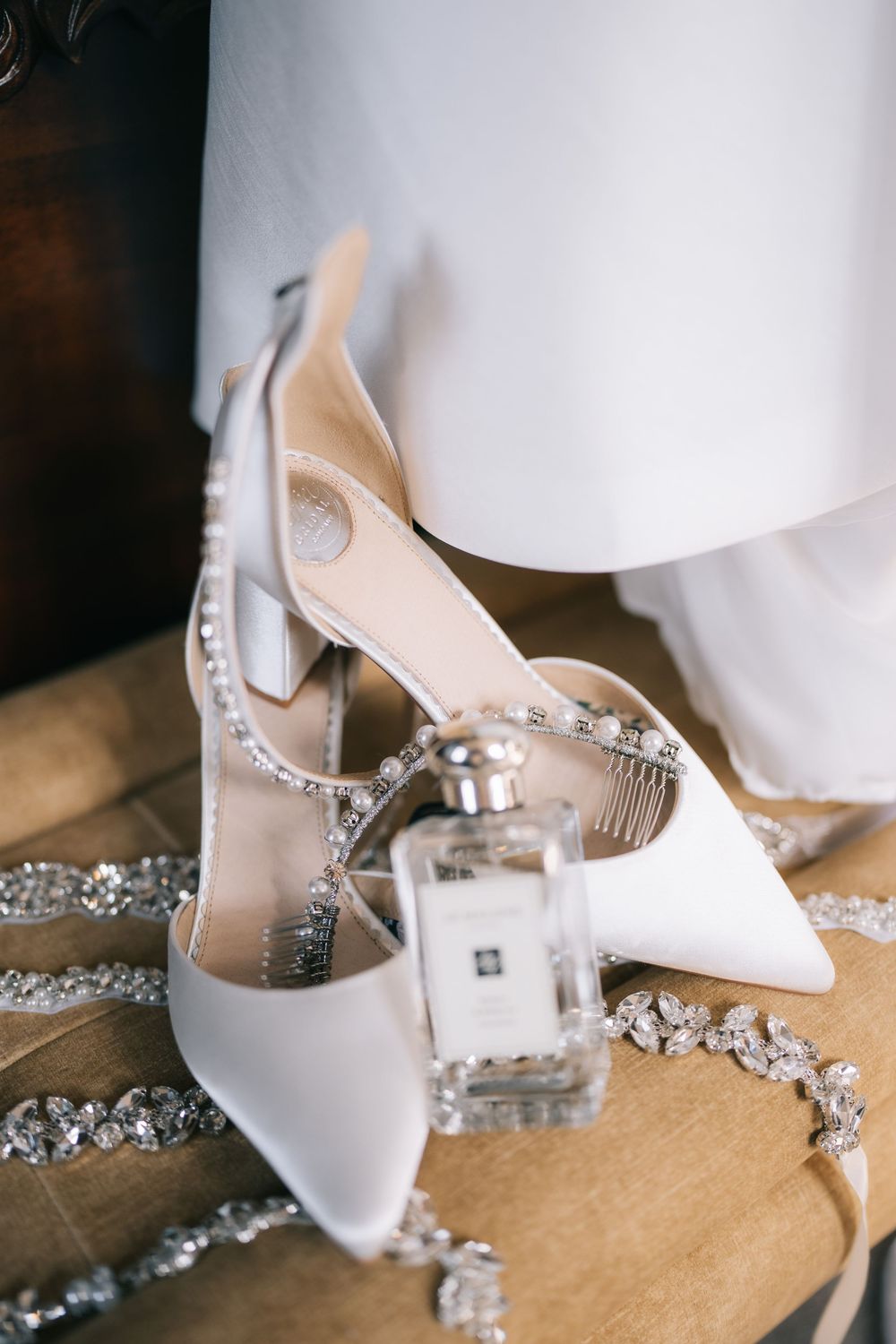 Elegant white bridal shoes with crystal embellishments and delicate straps displayed on a beige surface.