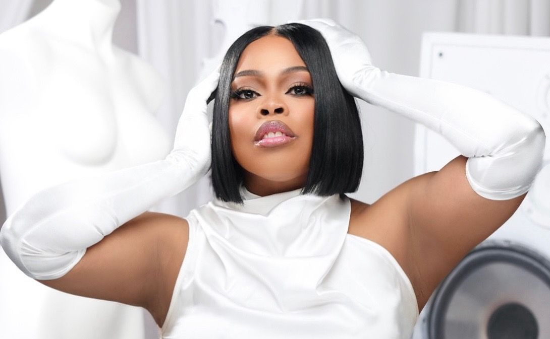 Stylish woman in white outfit and gloves posing confidently in a bright studio setting.