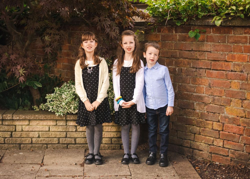 Children in formal attire pose against a brick wall outdoors.