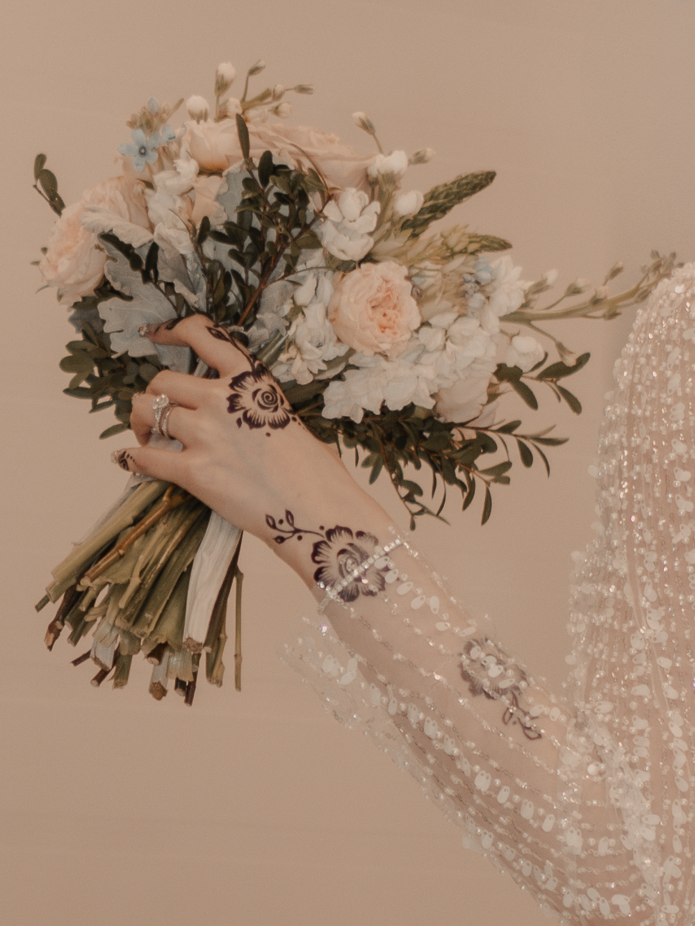 Soft-colored bridal bouquet with a bride's hand adorned in intricate henna designs.