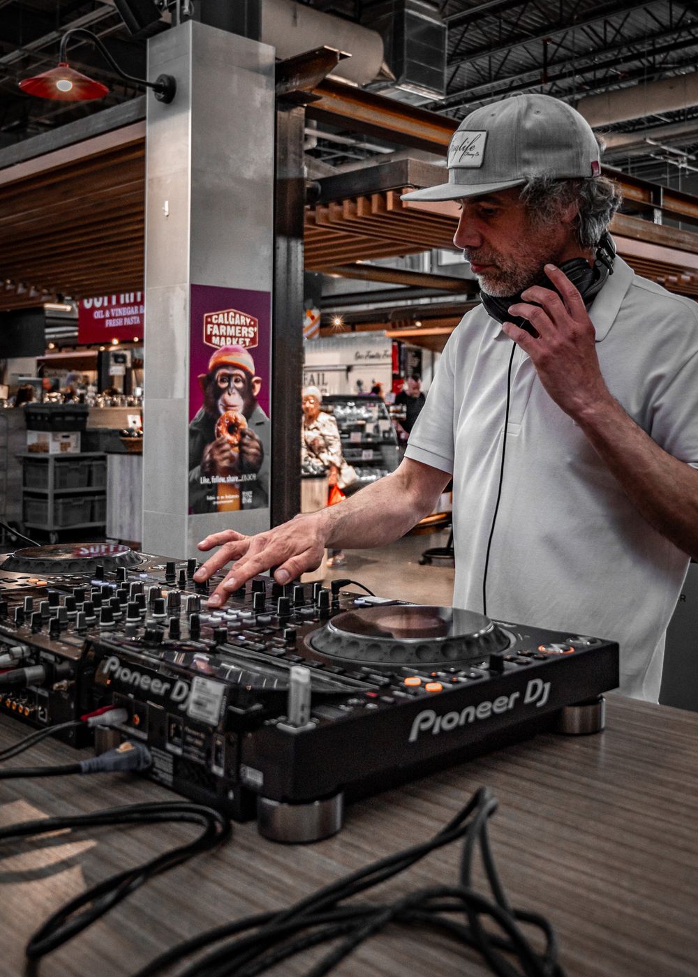 Male DJ performing indoors at Calgary Farmers Market, mixing tracks for a lively crowd.
