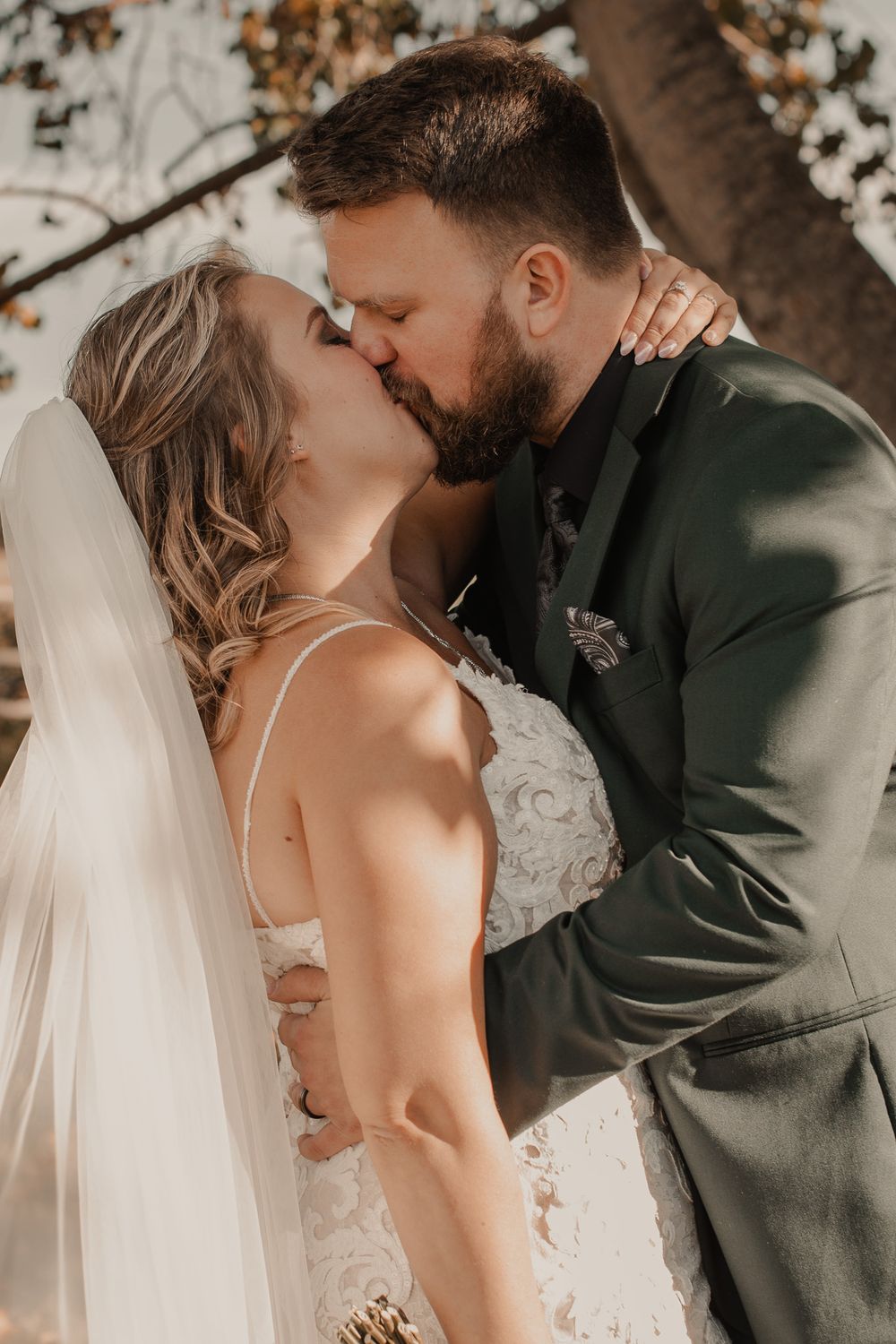 Bride and groom share their first kiss during a beautiful fall wedding ceremony, surrounded by vibrant autumn colors.