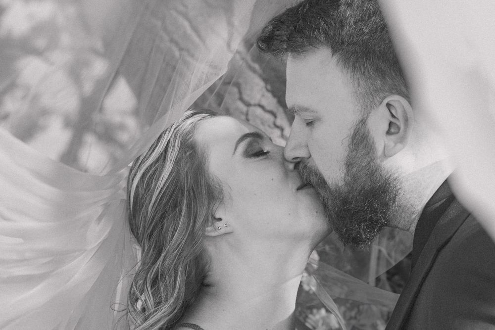 Bride and groom share a romantic kiss in a black and white photo, featuring the bride's veil softly in the background.