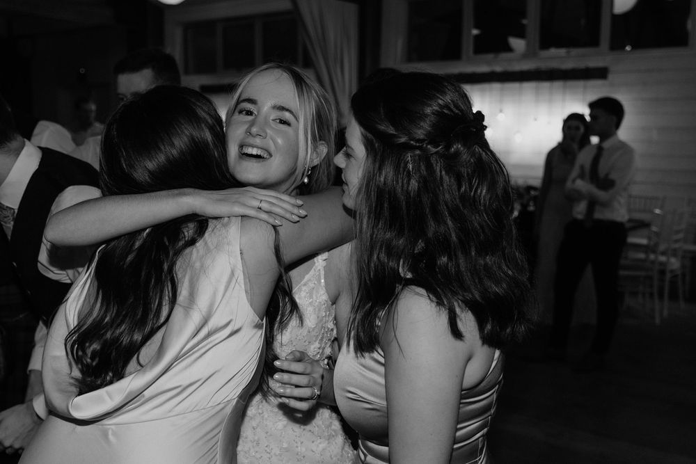 Wedding guests sharing an emotional group hug at a reception in black and white photography.