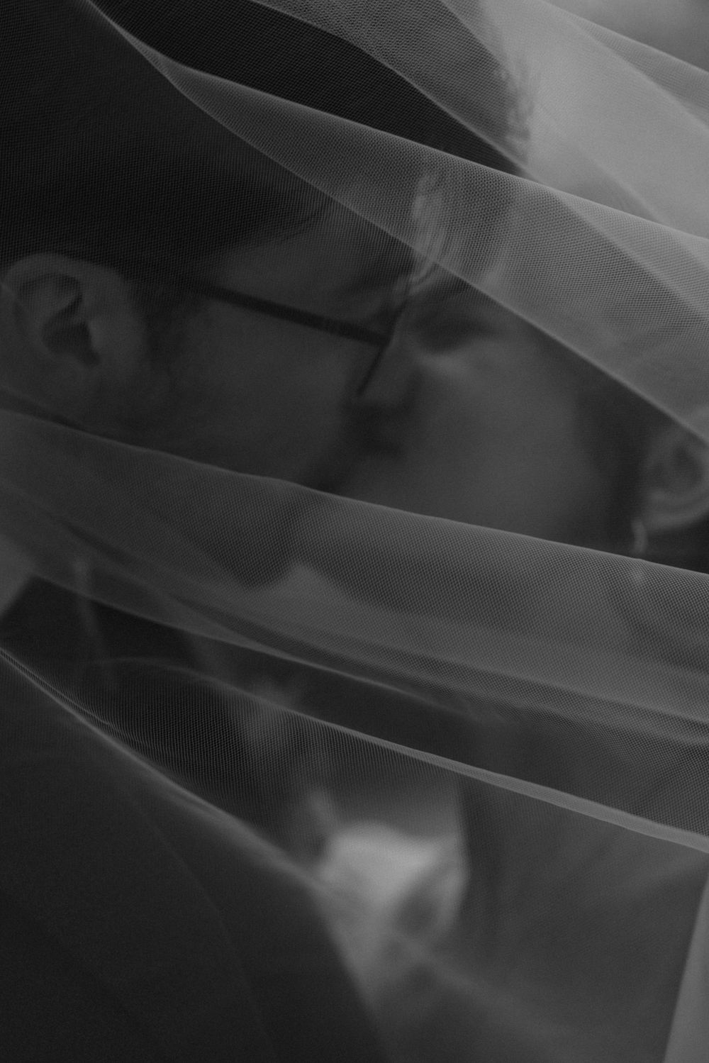 Artistic black and white photo of a couple kissing behind a flowing wedding veil.