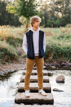 High school senior boy standing on a stone pathway in the middle of a river during fall.