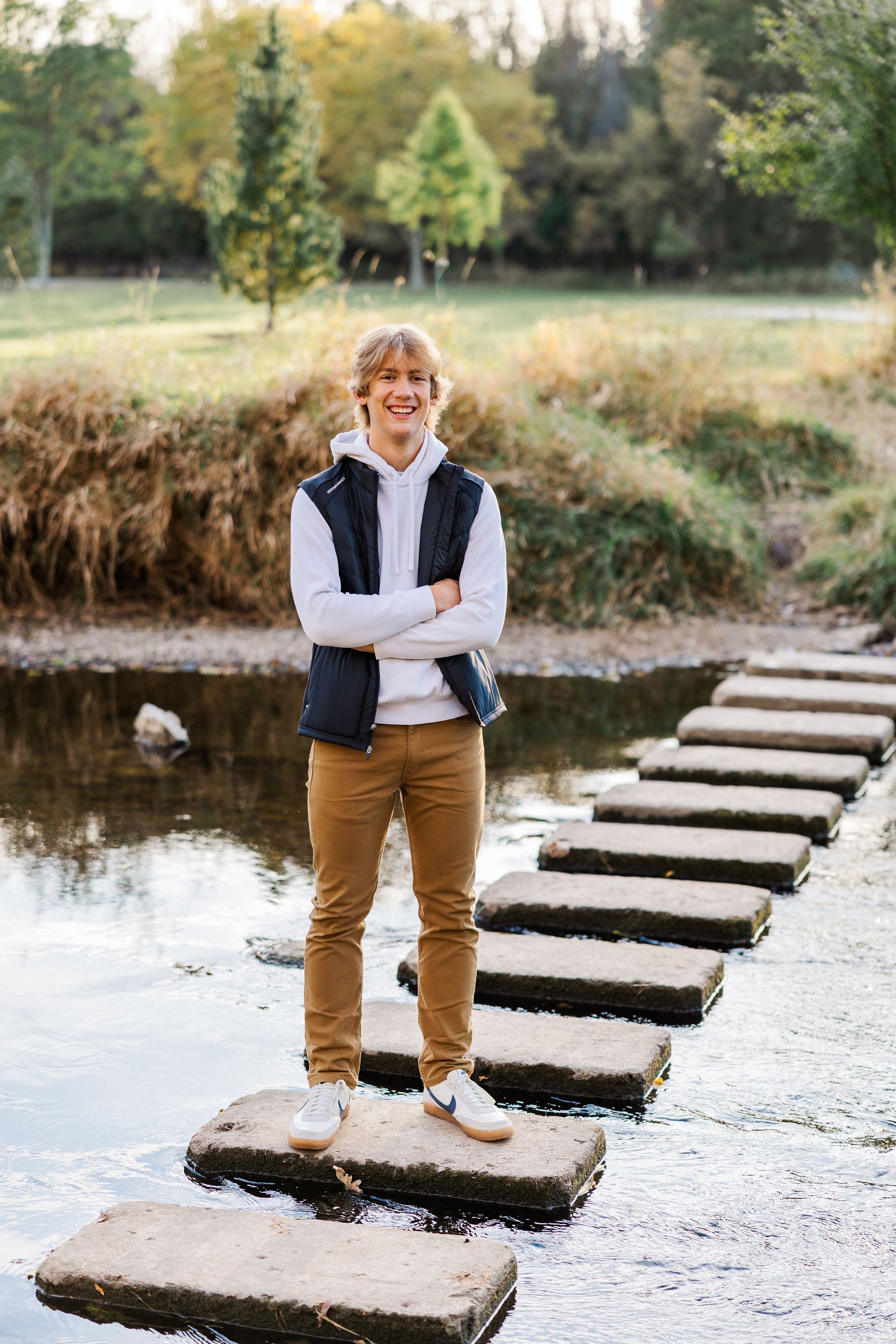High school senior boy standing on a stone pathway in the middle of a river during fall.