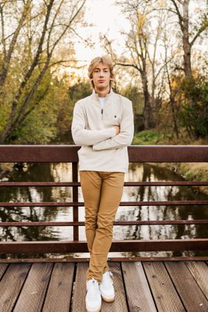 High school senior standing on a wooden and metal bridge surrounded by fall colors.
