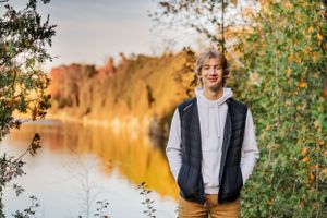 High school senior standing on the edge of a quarry surrounded by vibrant fall trees.