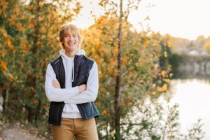 High school senior standing on the edge of a quarry surrounded by vibrant fall trees.