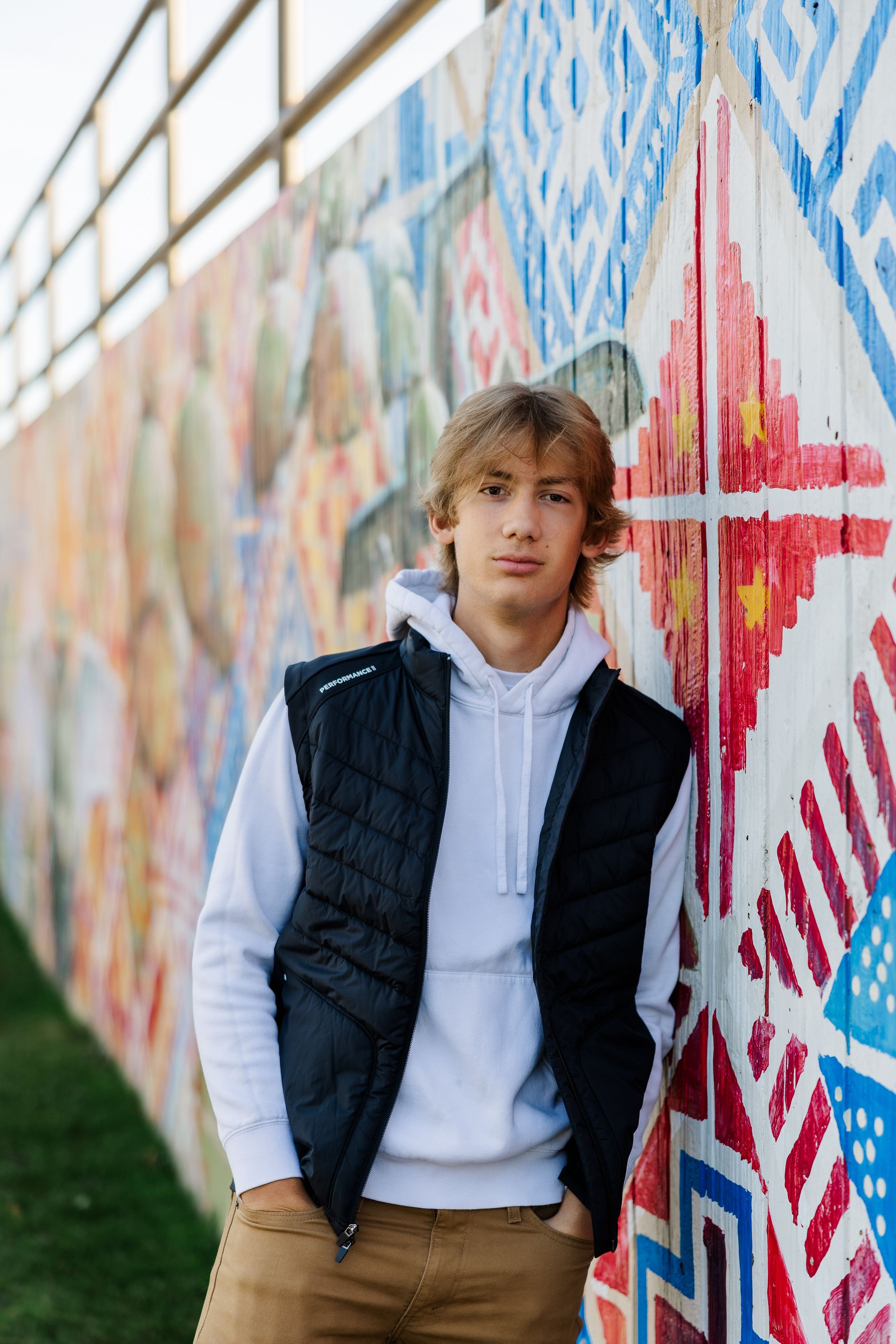 Highs school senior leaning against a painted wall in an urban setting.
