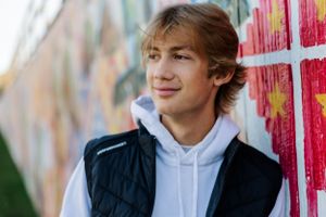 Highs school senior leaning against a painted wall in an urban setting.