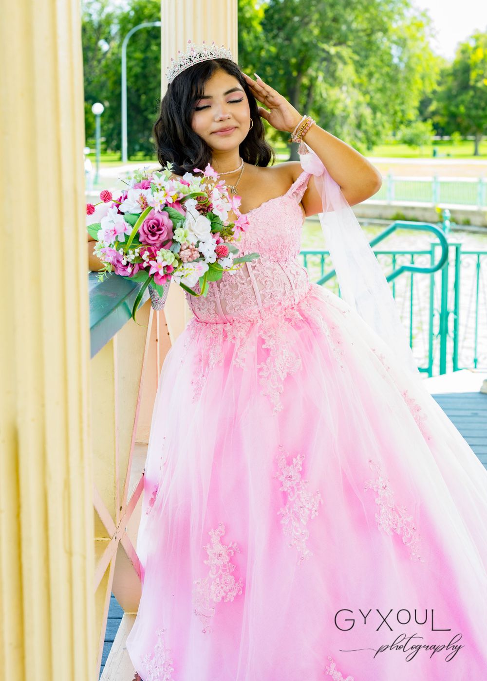 A portrait on a deck showing a pink ball gown and floral bouquet against a natural backdrop.