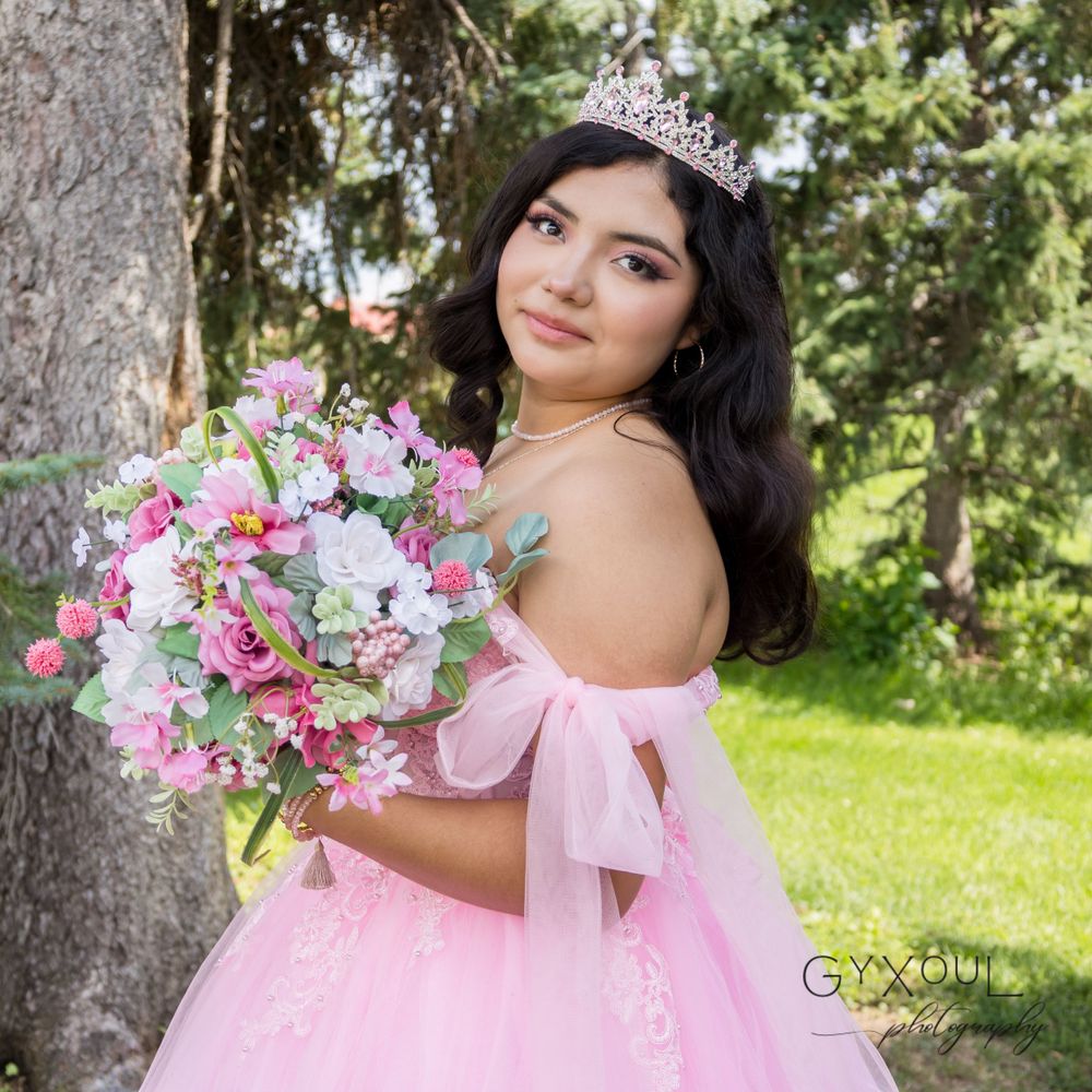 A quinceañera celebration photoshoot featuring a pink tulle gown and floral bouquet in an outdoor garden setting.