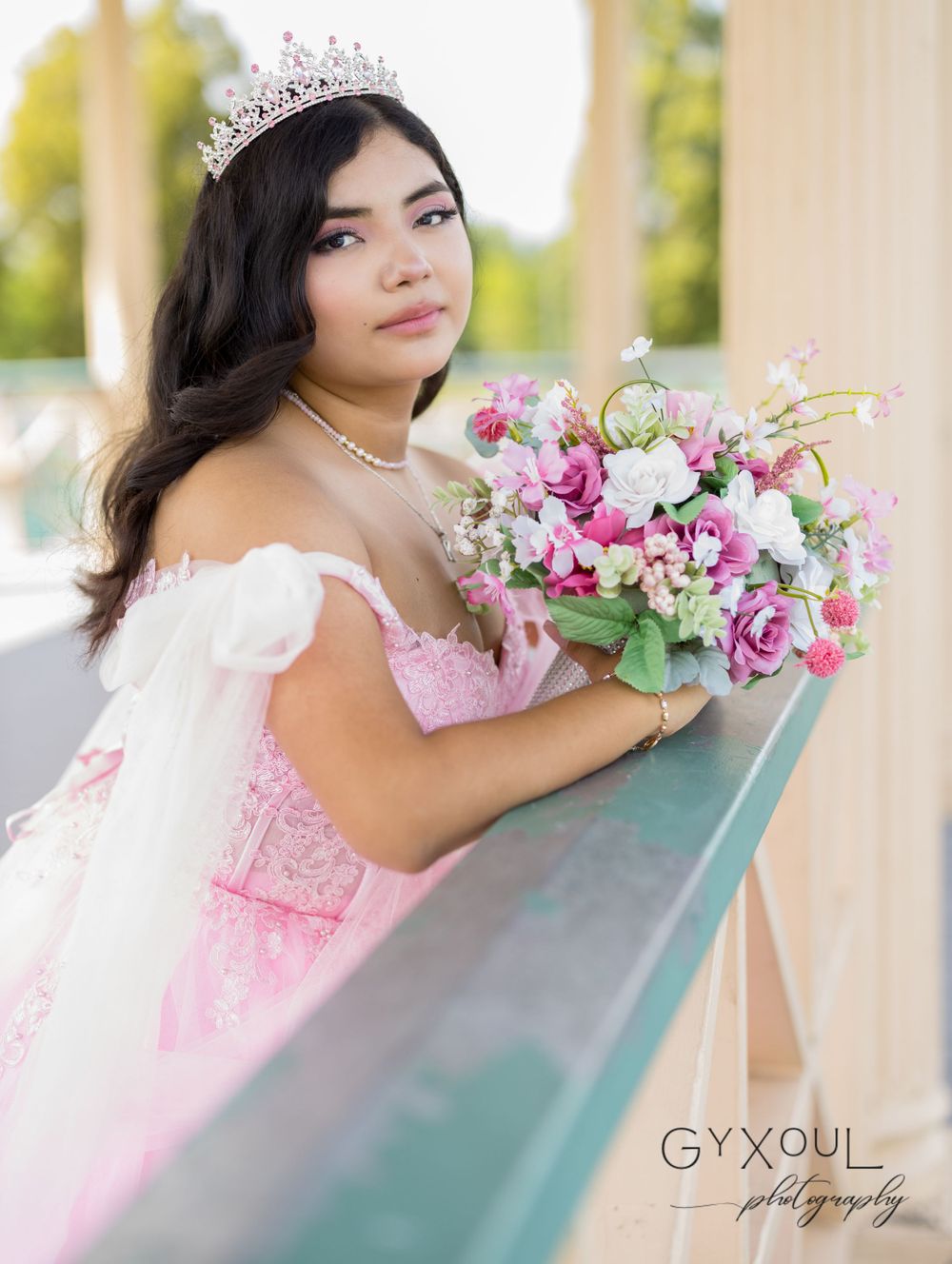 A formal portrait of someone wearing a pink ball gown and tiara while holding a colorful floral bouquet.