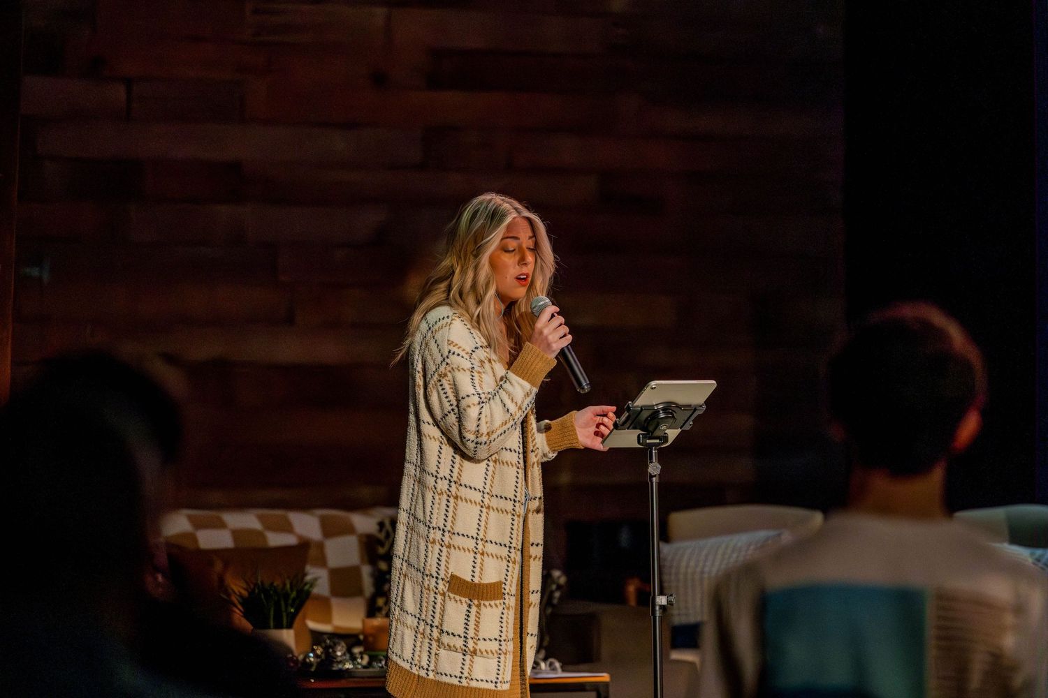 A speaker presents from a podium in a dimly lit room with wooden walls.