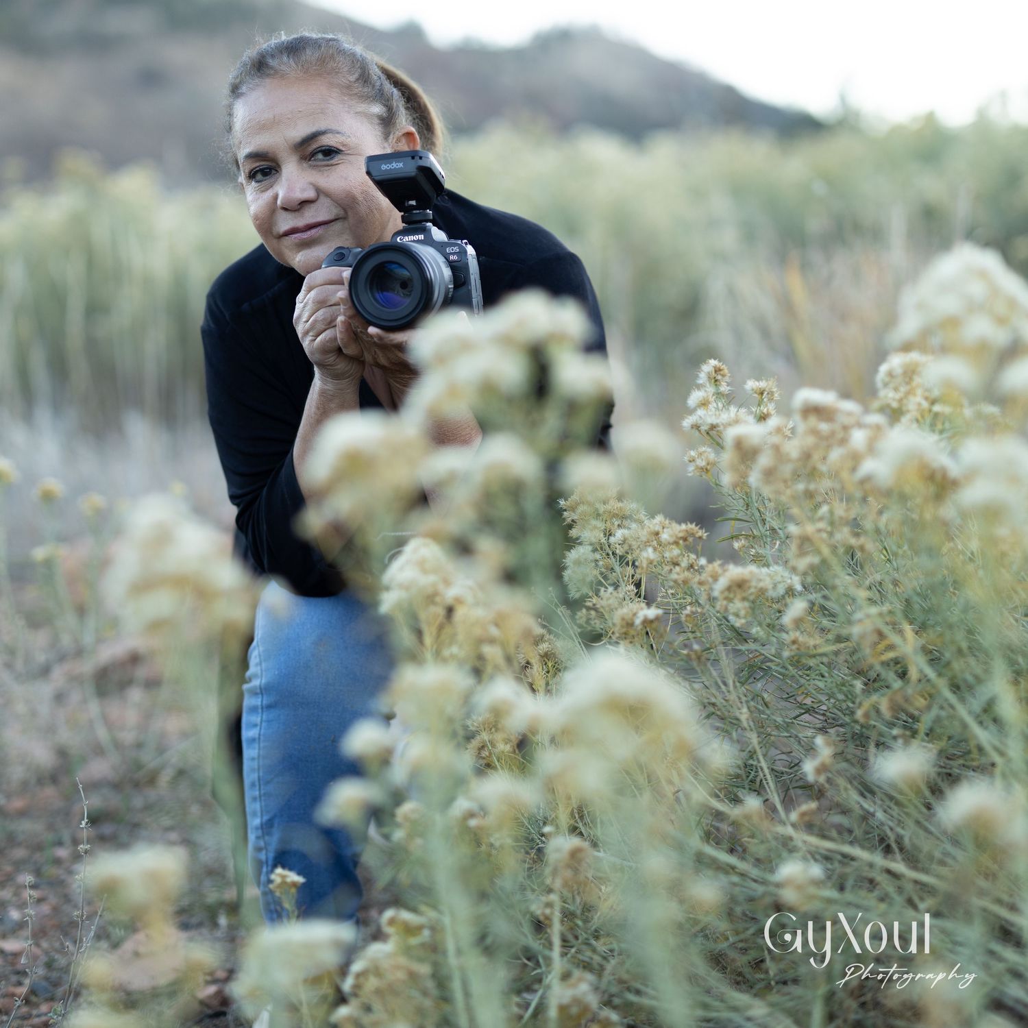 Photographer in the wilderness capturing photos among tall yellow wildflowers at sunset.