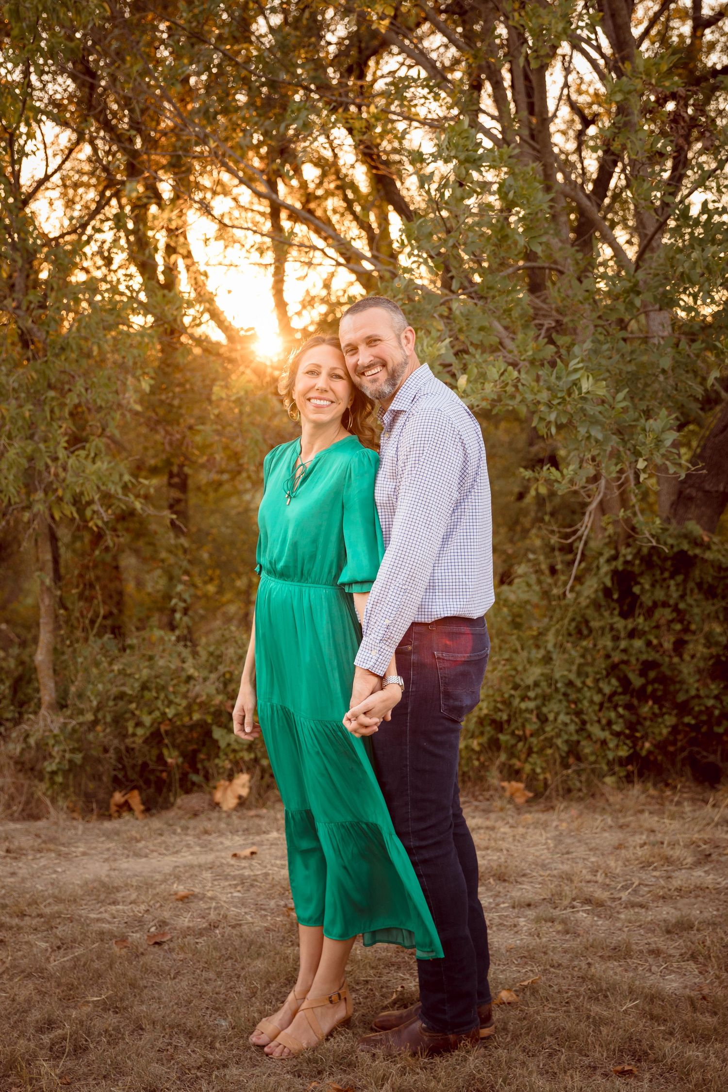 Couple sitting together at sunset in outdoor setting with golden light filtering through trees.