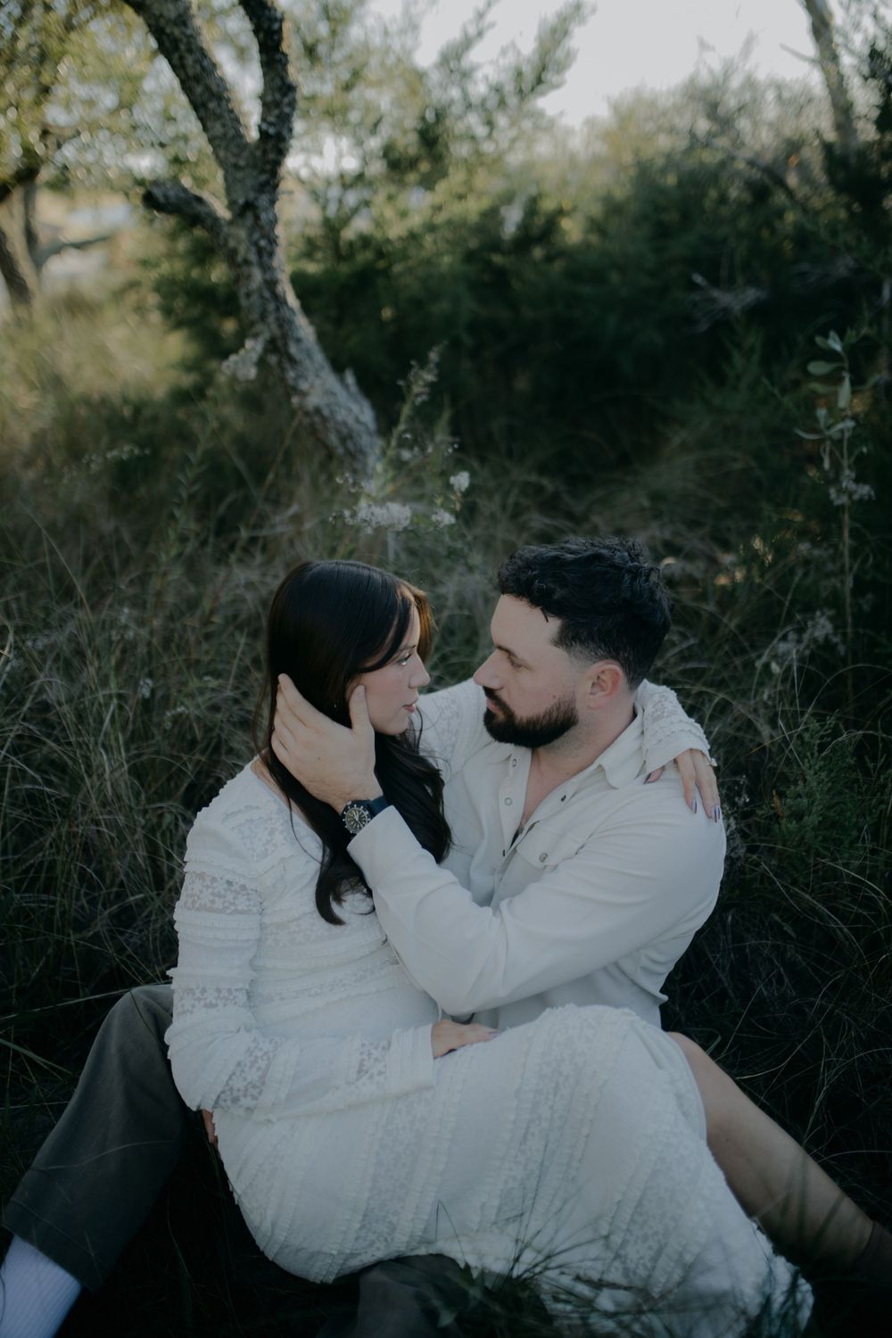 Couple in white clothing sharing an intimate moment in a natural setting.