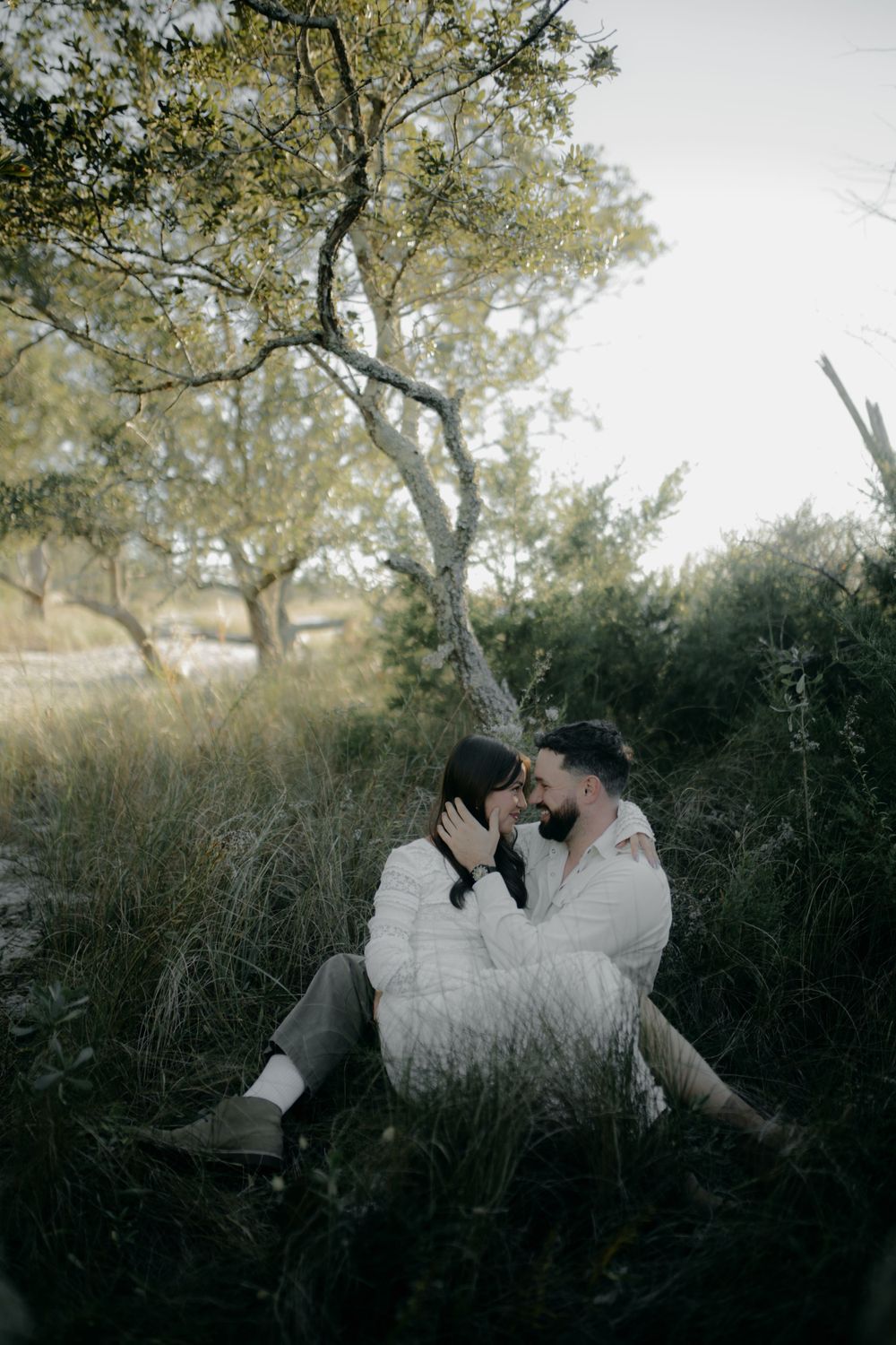 Couple in white clothing lying together in tall grass during golden hour.