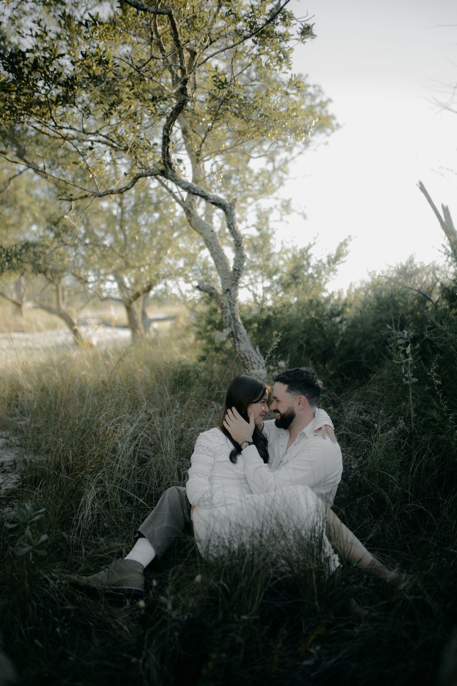 Couple in white clothing lying together in tall grass during golden hour.