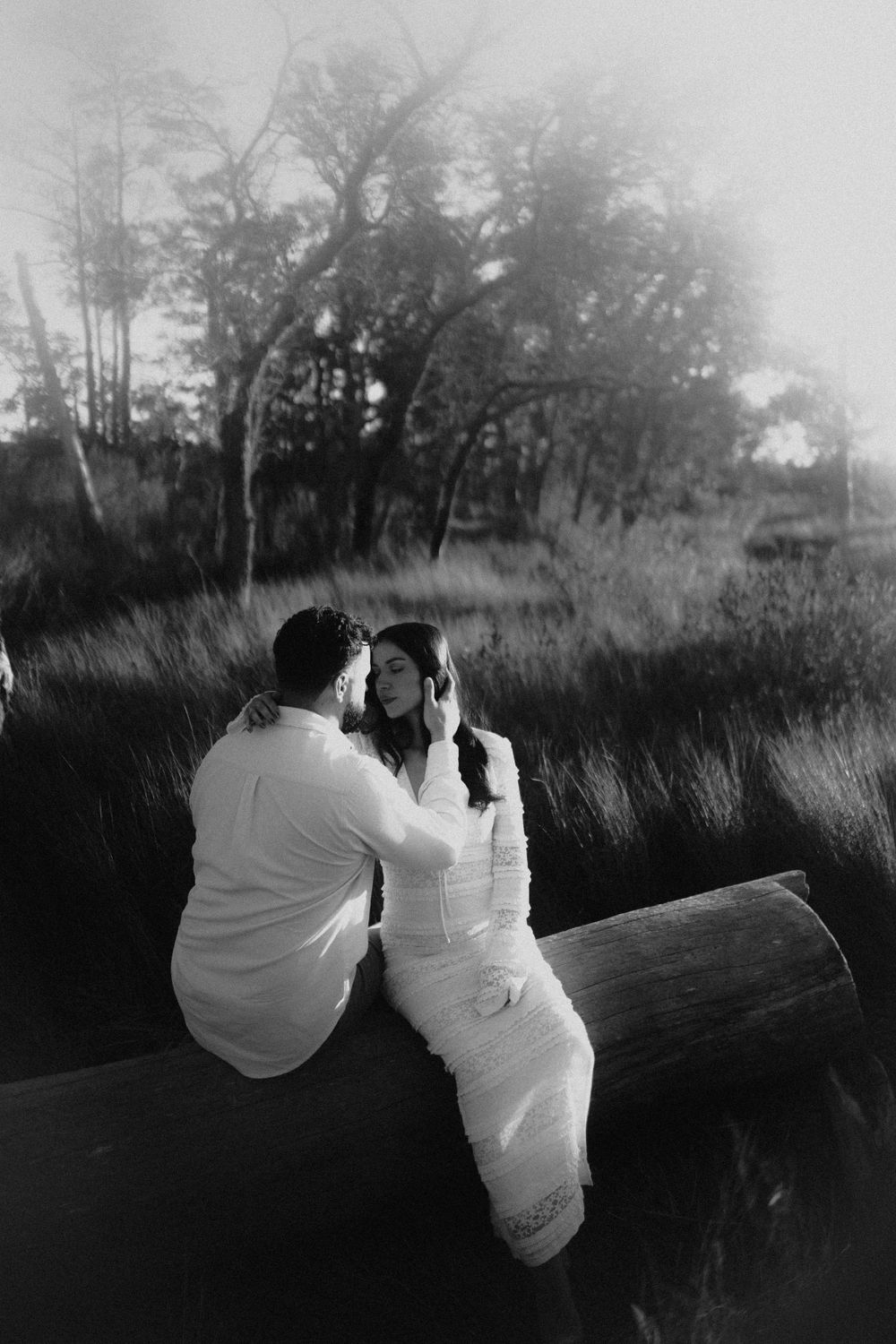Black and white photo of two people in white clothing sitting together in a grassy field.