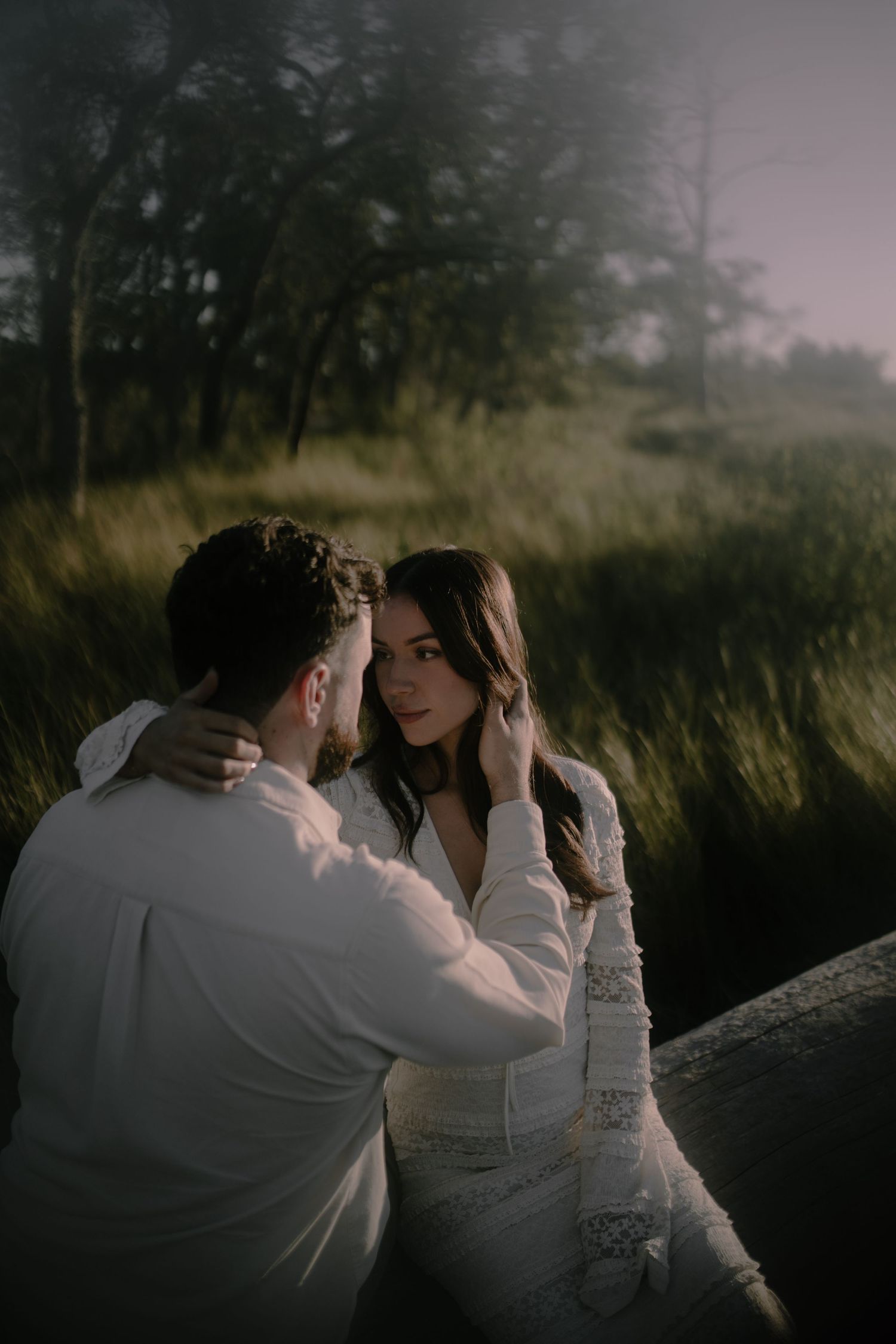 An intimate moment captured between a couple in a misty field at dusk.