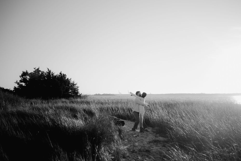 A couple embracing in a field of tall grass during sunset with a dreamy black and white filter.