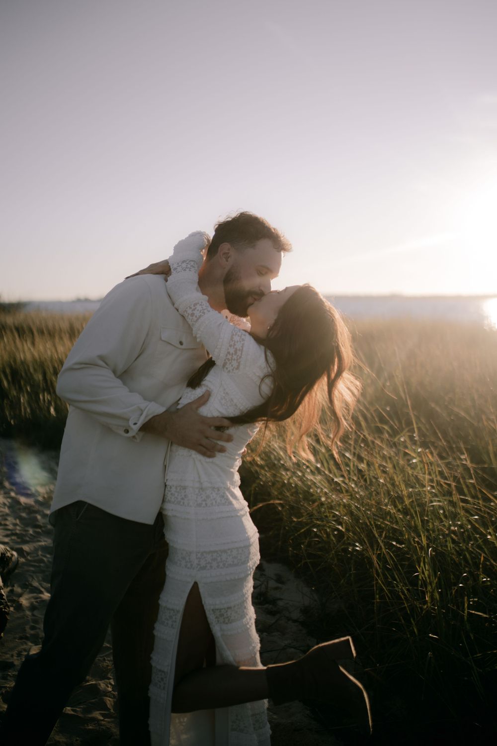 A tender embrace between a couple in formal wear against a golden sunset backdrop.
