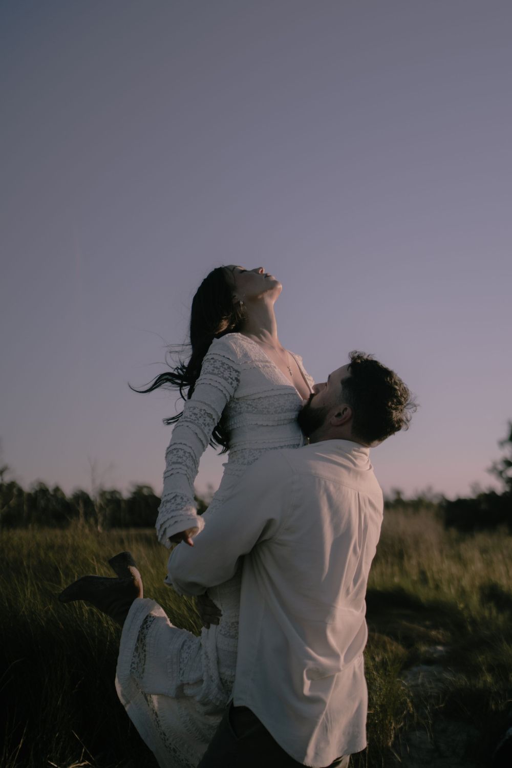 A couple sharing a playful moment with a lift pose in a field at sunset.