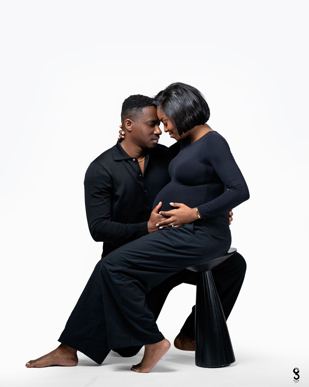 Two people in black clothing dance together in an intimate contemporary dance pose against a white backdrop.
