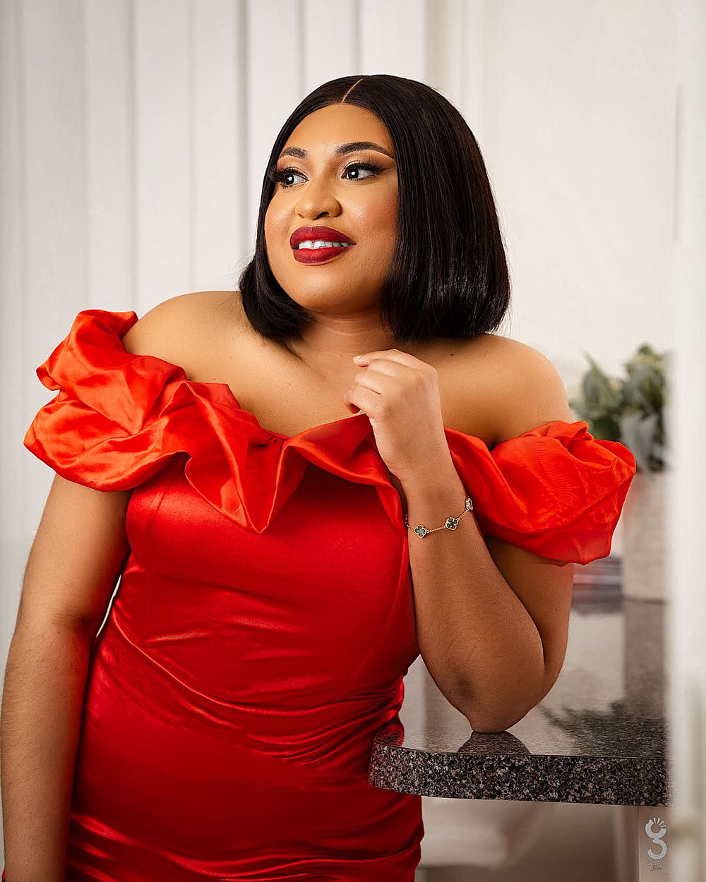 Woman wearing a dramatic red off-shoulder gown poses for elegant portrait.