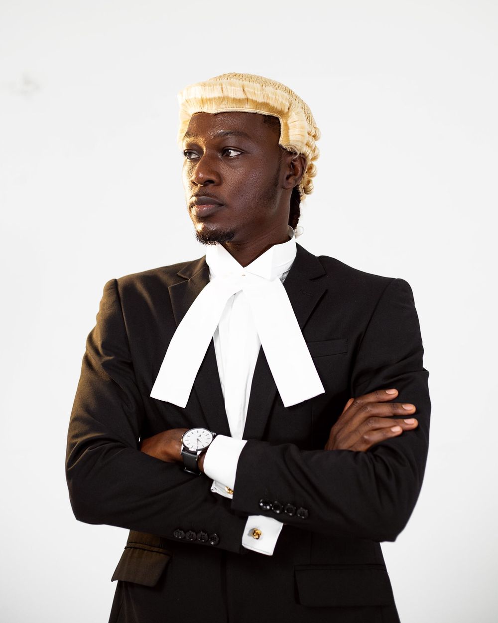 A barrister poses confidently in traditional legal attire with crossed arms against white background.