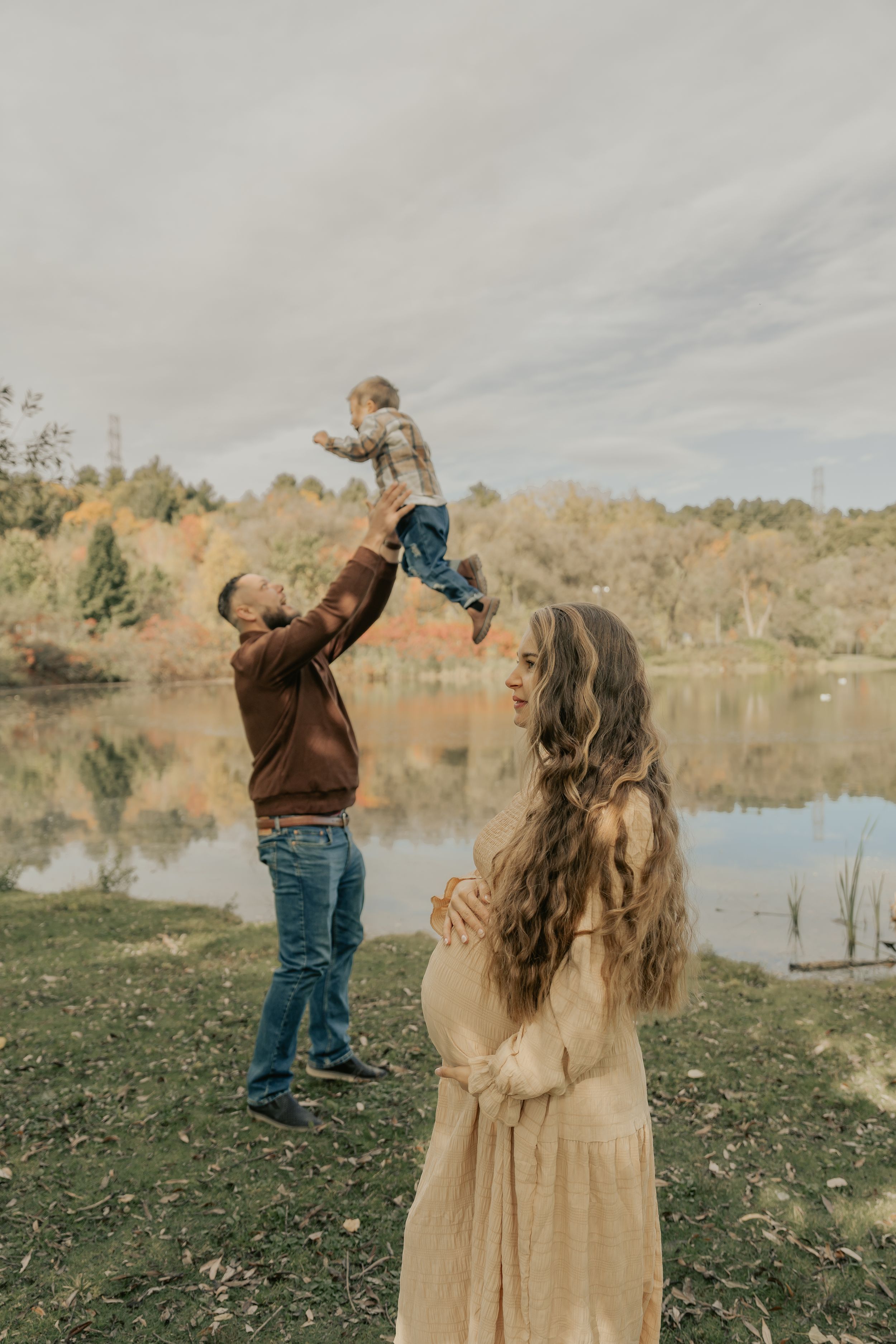 A family enjoys an autumn afternoon by a lake with fall foliage in the background.
