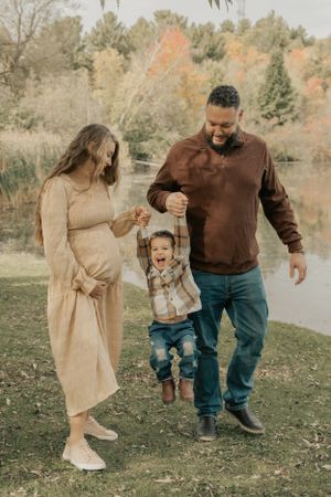 A playful family scene outdoors with fall colors and a lake in the background.