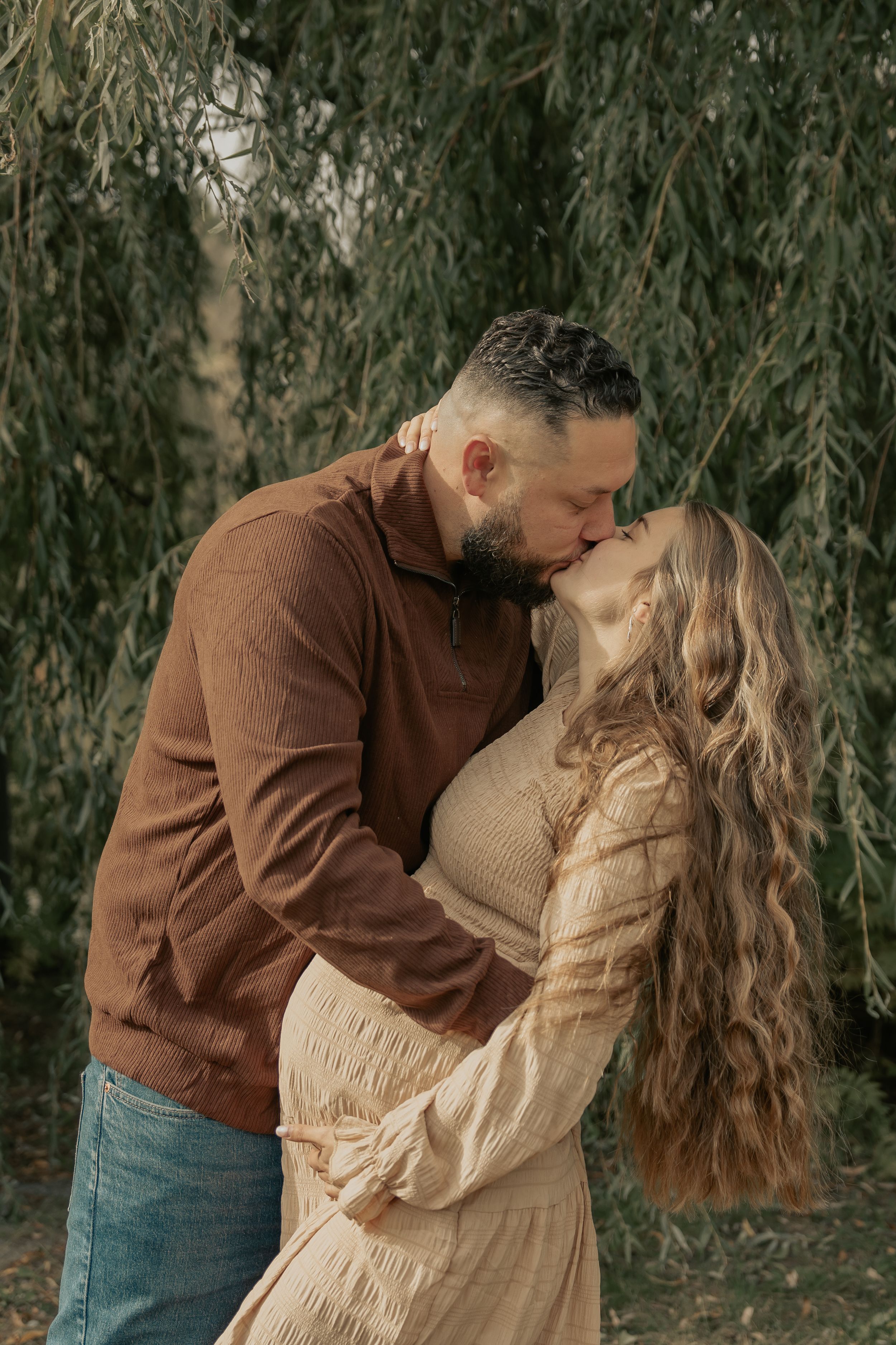 A romantic maternity photo beneath willow trees during autumn.