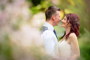 Romantic wedding portrait captured through soft focus flowers in a garden setting.