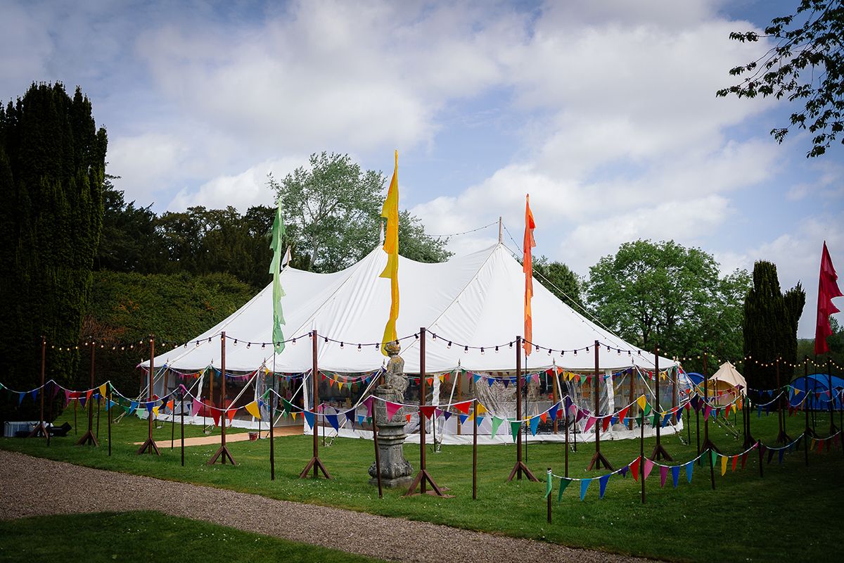 Panoramic view of white wedding tent decorated with colorful flags and bunting in outdoor setting.