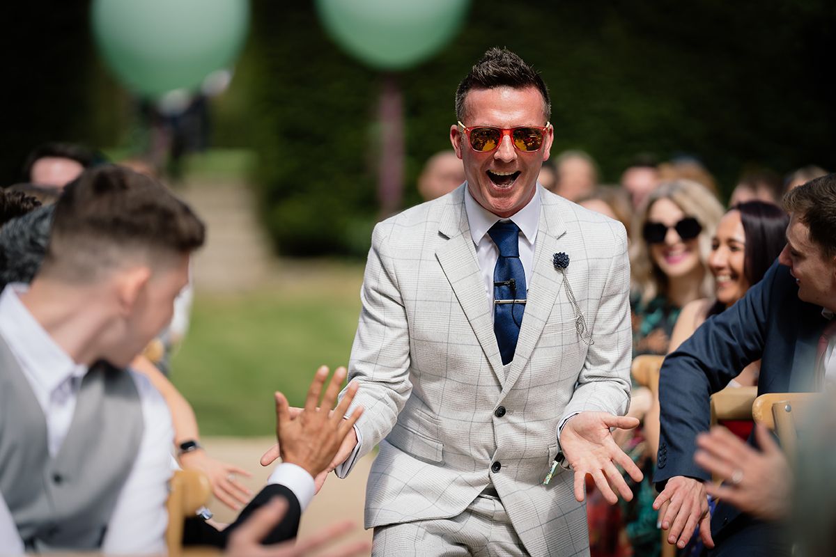 Wedding party celebrates with energetic dance moves in a garden setting.