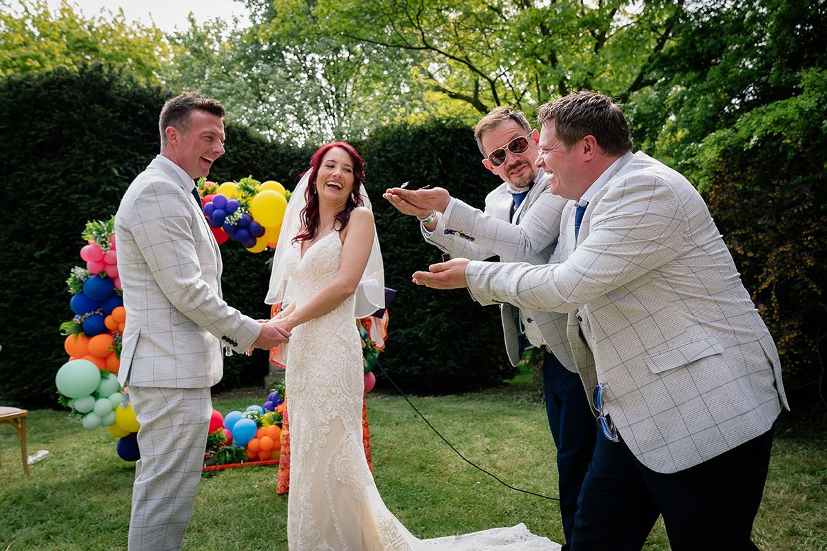 Wedding celebration with guests dancing and laughing in a sunny outdoor venue.