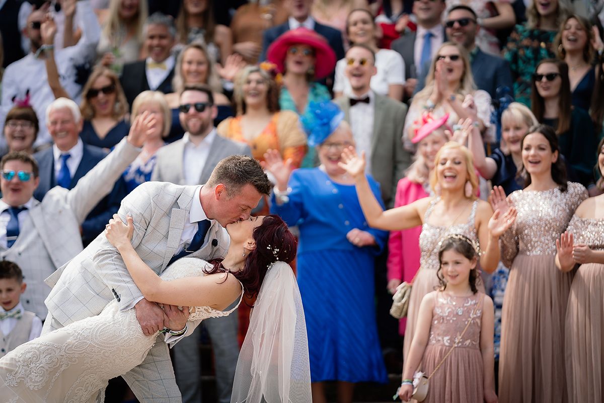 Wedding guests cheer and celebrate during an outdoor reception with colorful attire.