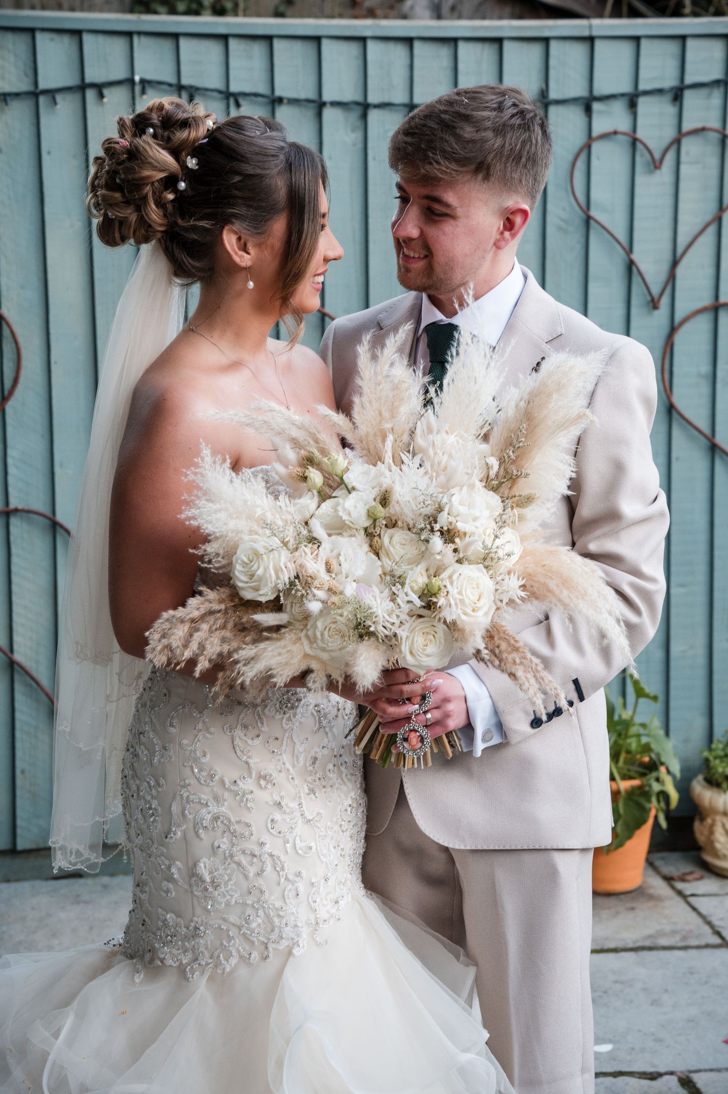 A romantic wedding couple in white attire share tender moments while holding a beautiful pampas grass and floral bouquet.