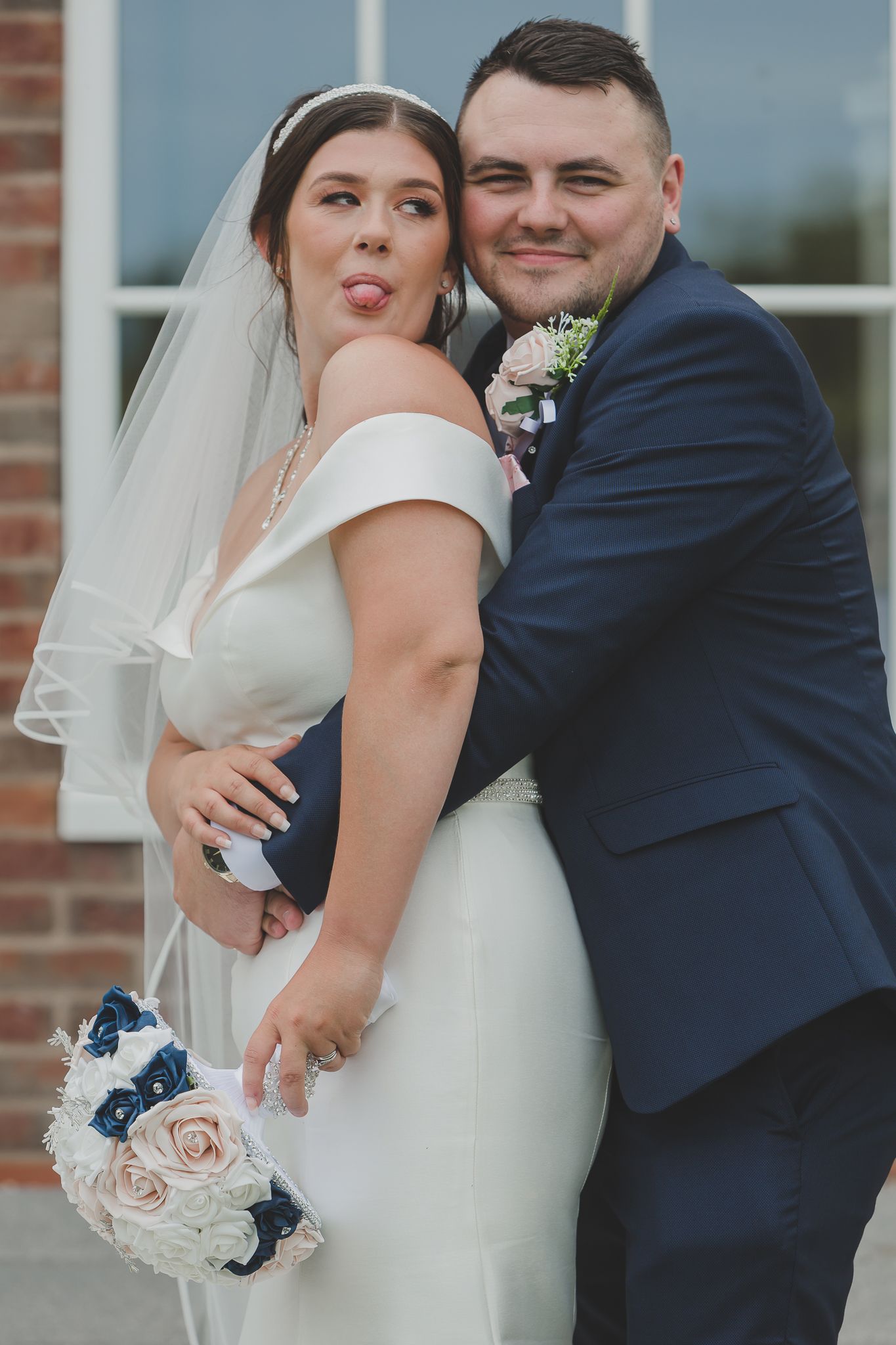 Newlyweds share playful moments in front of brick building.