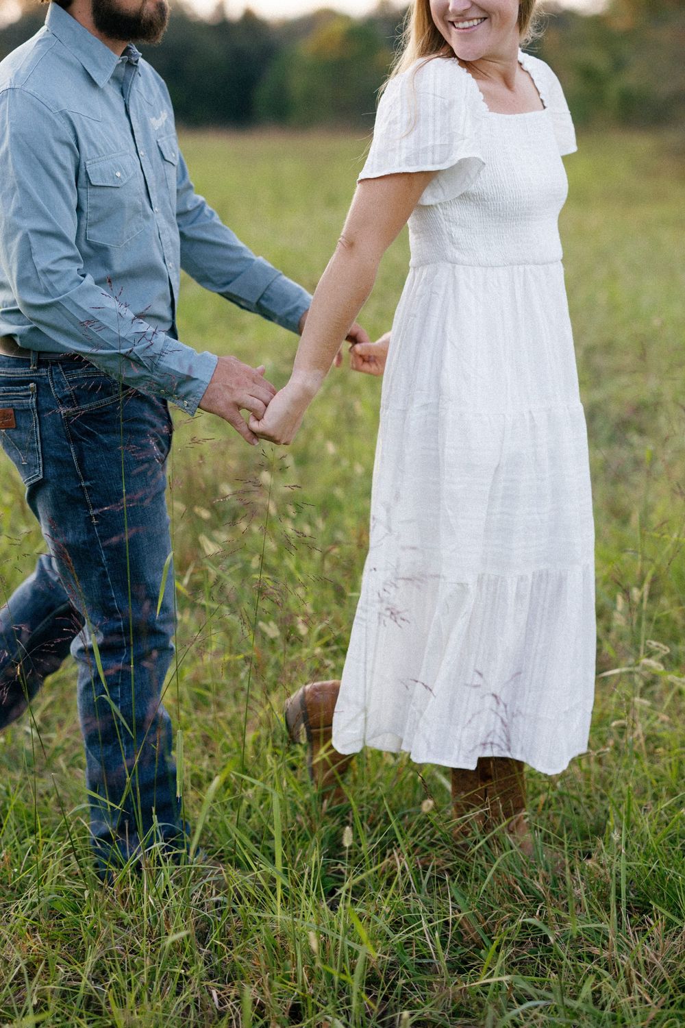 A couple in casual attire stands together in a grassy meadow on a sunny autumn day.