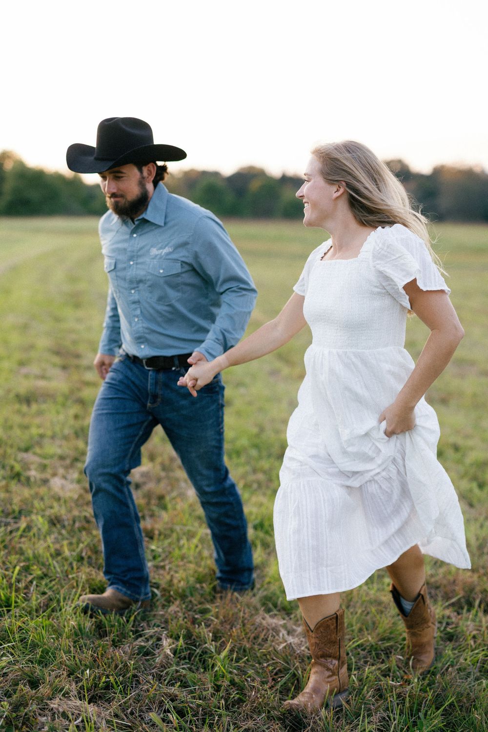 A couple dances and twirls together in a sunlit meadow wearing cowboy boots and casual attire.