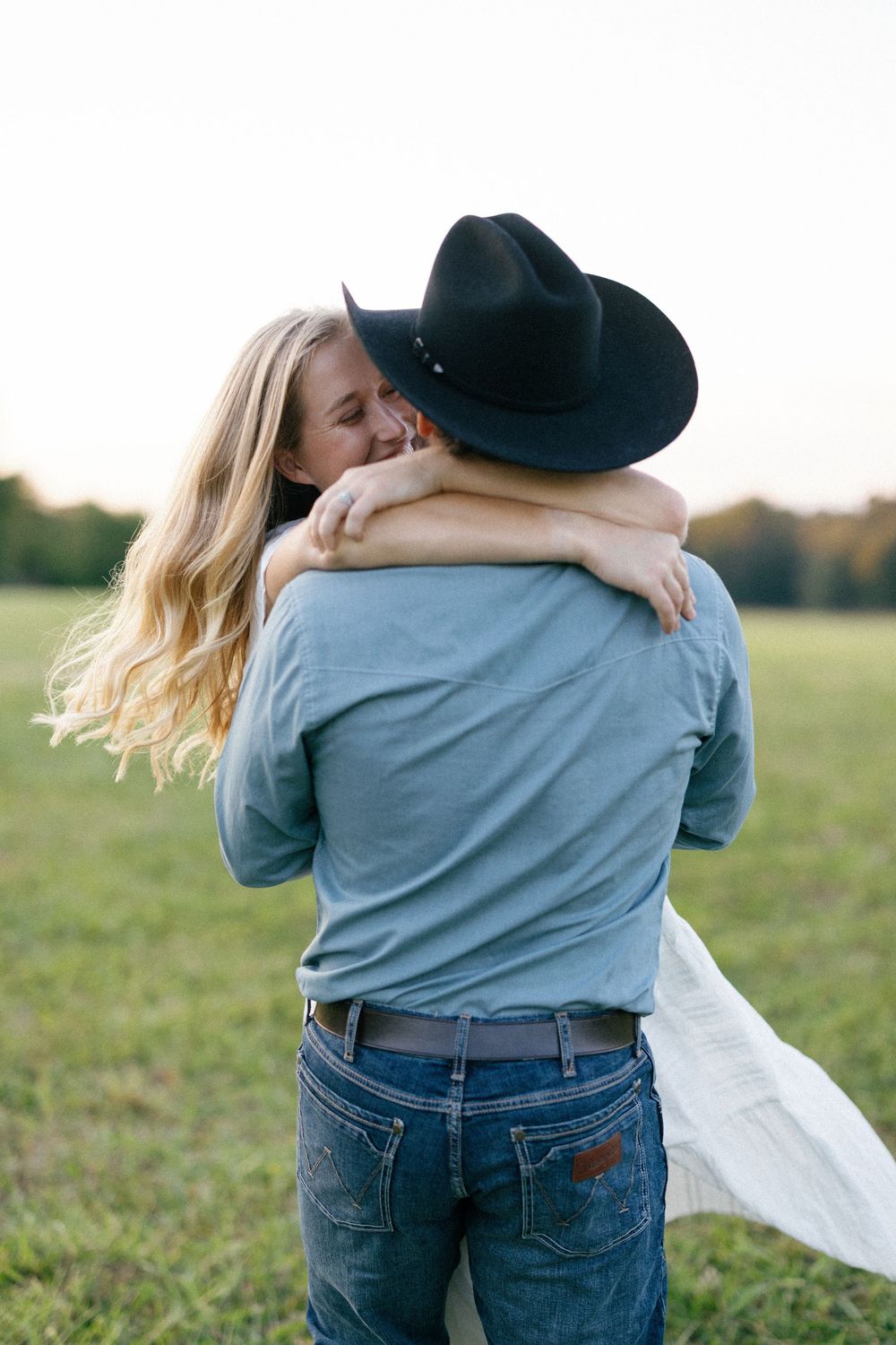 A romantic embrace captured in a field with flowing white dress and denim details.