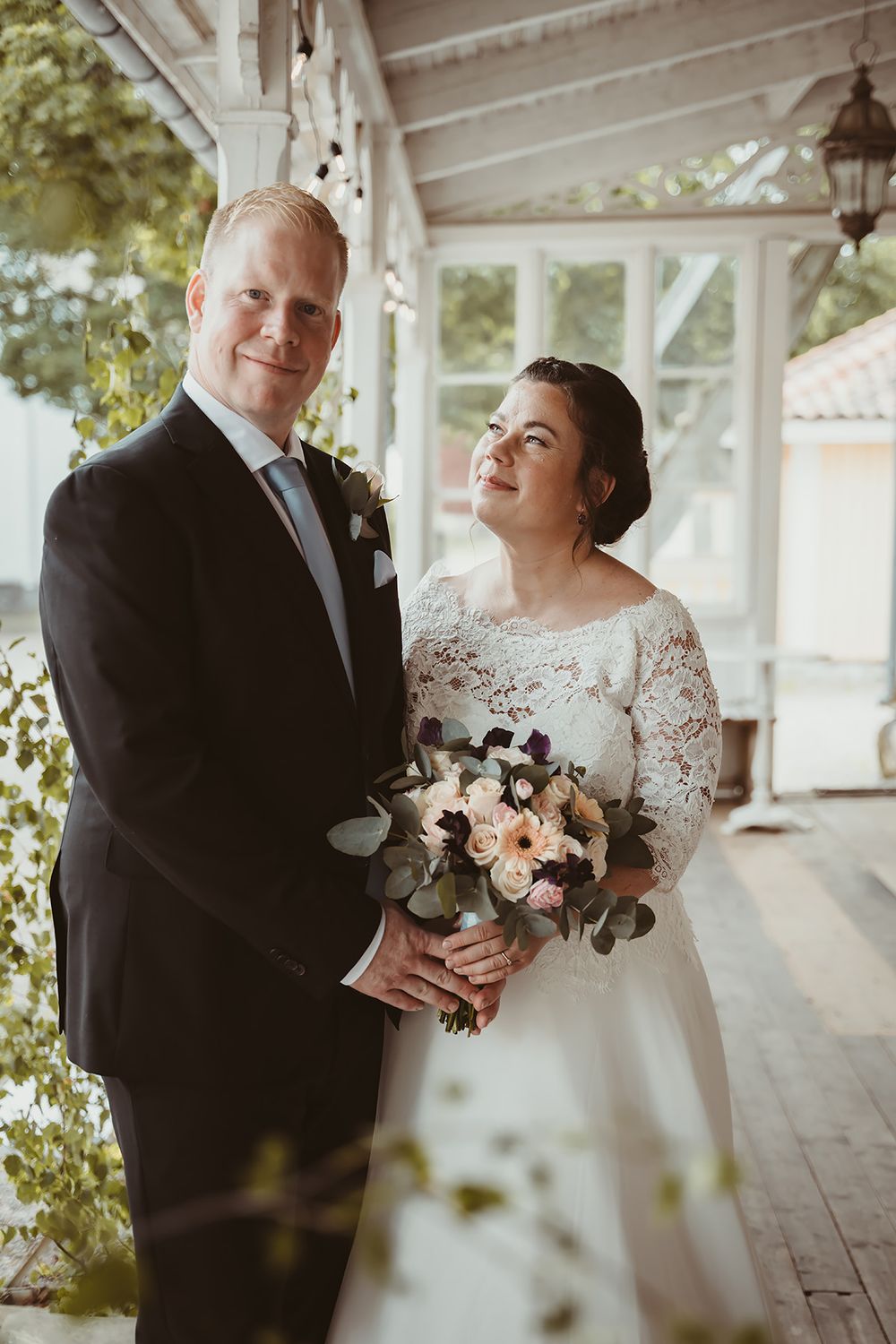 Brudporträtt, en fotografering av brudpar ståendes på en vacker vit veranda under en bröllop i Östergötland. Fotograd Josefin Landhagen.