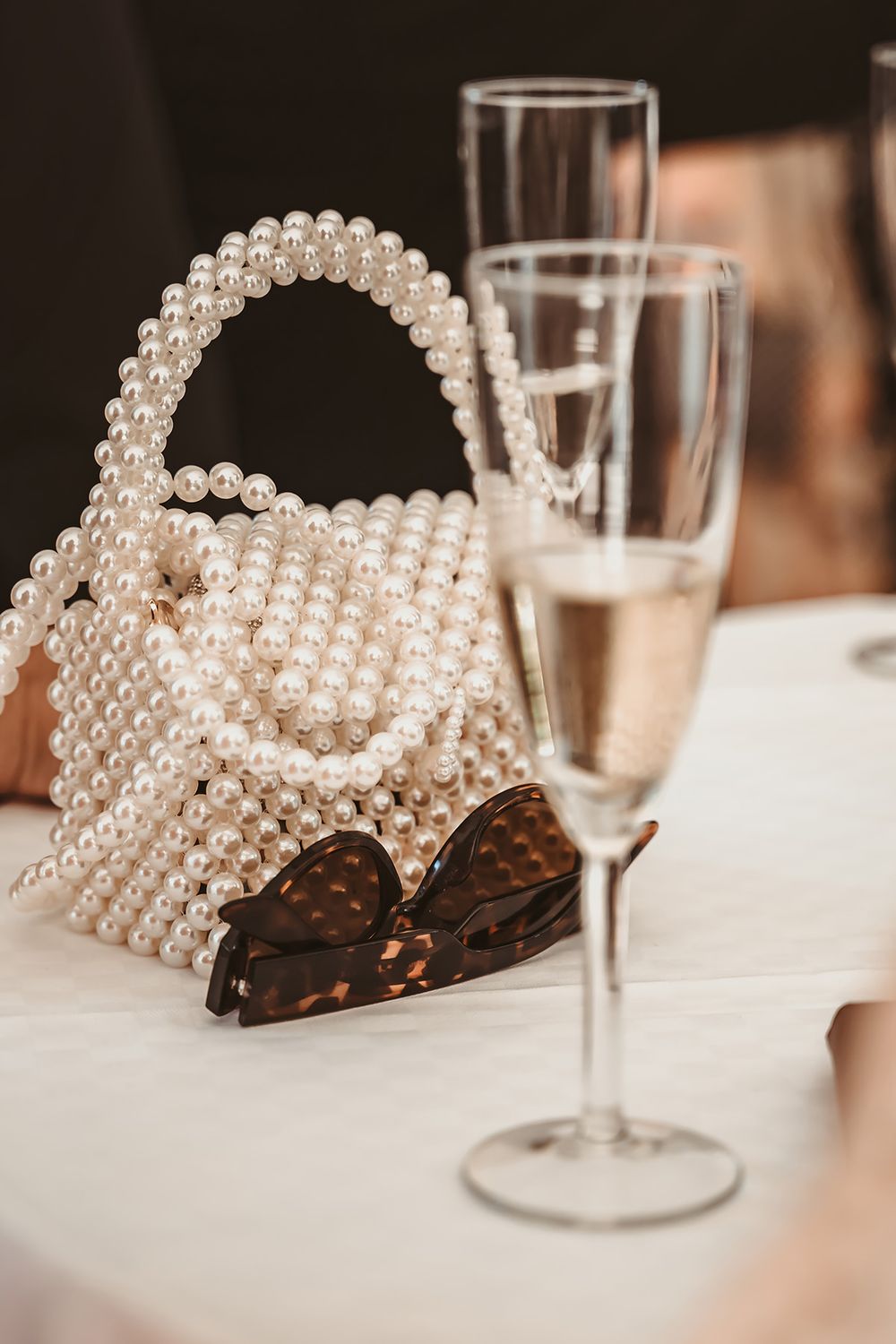 Detaljfoto på en väska av vackra pärlor ståendes intill ett champagneglas under ett bröllop i Östergötland, bröllopsfoto av Lets Bloom Media