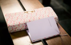 A floral patterned fabric or paper being cut with scissors on a dark surface.