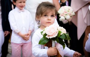 A group of people in formal attire gather at a wedding celebration with pink and white floral arrangements.